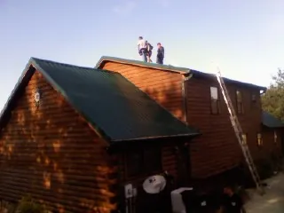 Crew on the ridge of a green metal roof on a two story log home in Rio Vista