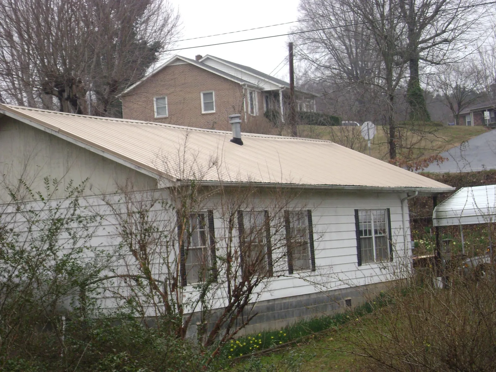 Tan metal roof on a white sided house set into a hillside — Commercial Roofing by Roofing Brothers in Rio Vista